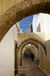 Image du Maroc Professionnelle de  Dans une rue des Habous, la succession des balèvres, moulure, arches, portiques et autres éléments décoratifs, projetent les visiteurs dans l’ardeur avec un élan de force et de fierté d’une époque révolue. Conçu par les architectes Auguste Cadet et Edmond Brion d’après l’ébauche d’un premier plan-masse dû à Albert Laprade, le quartier fait partie des endroits les plus pittoresques de Casablanca, il fut La construction n’avait commencé qu’après la première guerre mondiale. Situé près du Palais Royale, ce joyau architectural fait partie du patrimoine architectural de la ville, Samedi 8 Novembre 2008. Au centre le minaret de La mosquée Ben Youssef. (Photo / Abdeljalil Bounhar)
